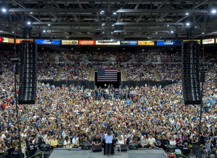 A large crowd fills an arena, watching a politician speak on stage.