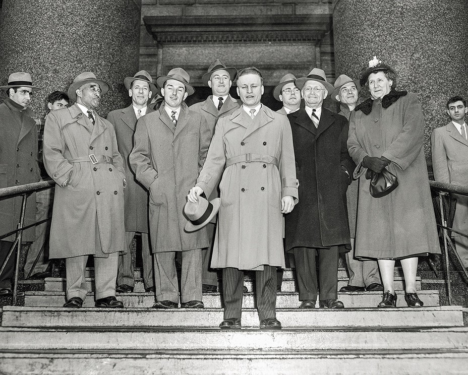 black and white photo of group of men wearing trench coats and hats with one woman holding handbag