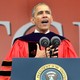 Barack Obama stands at a microphone wearing a graduation gown.
