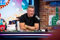 Photo of Pat MacAfee sitting behind a desk with his arms folded, speaking into a microphone