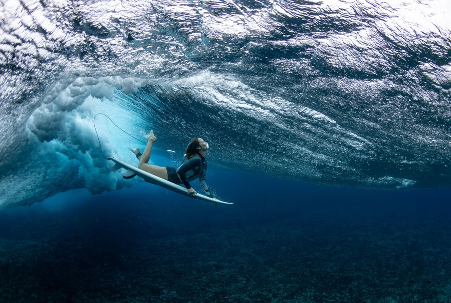 A surfer dives beneath a wave, seen underwater.