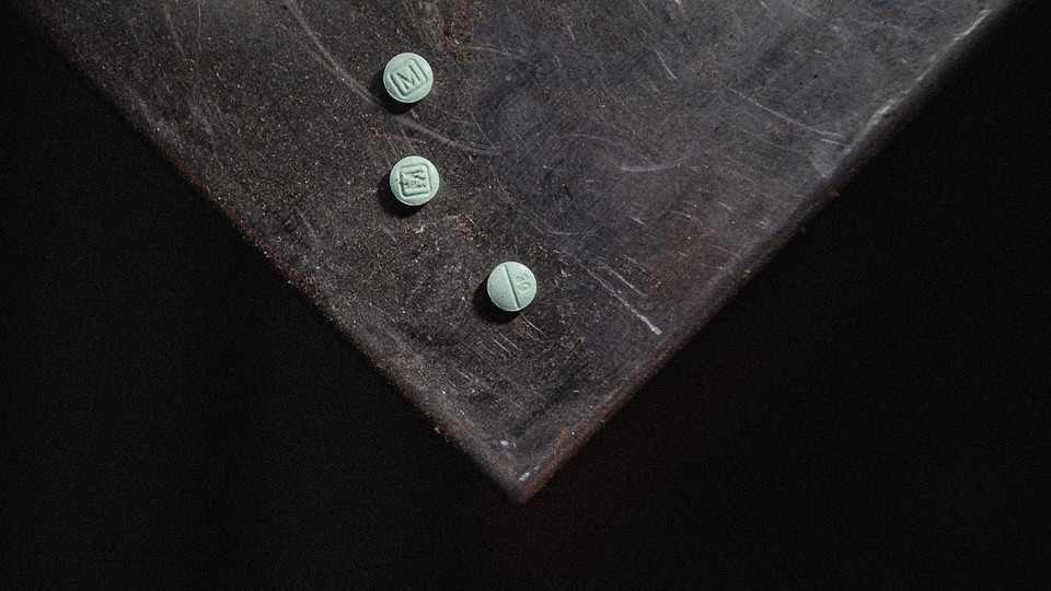 A color photograph of a black, scuffed service with three small, teal-colored pills on top.