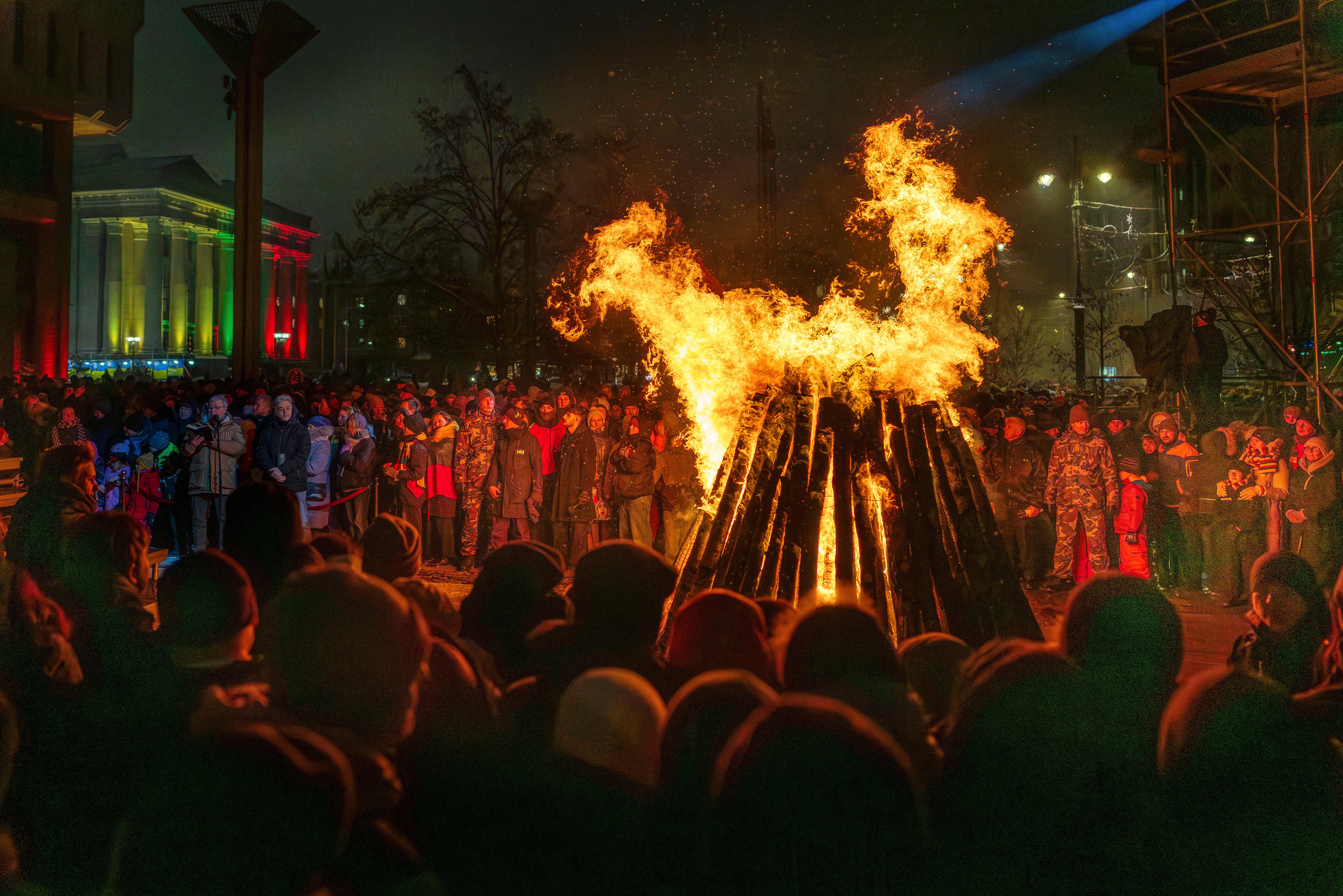 People watch a bonfire, gathered in a public square.