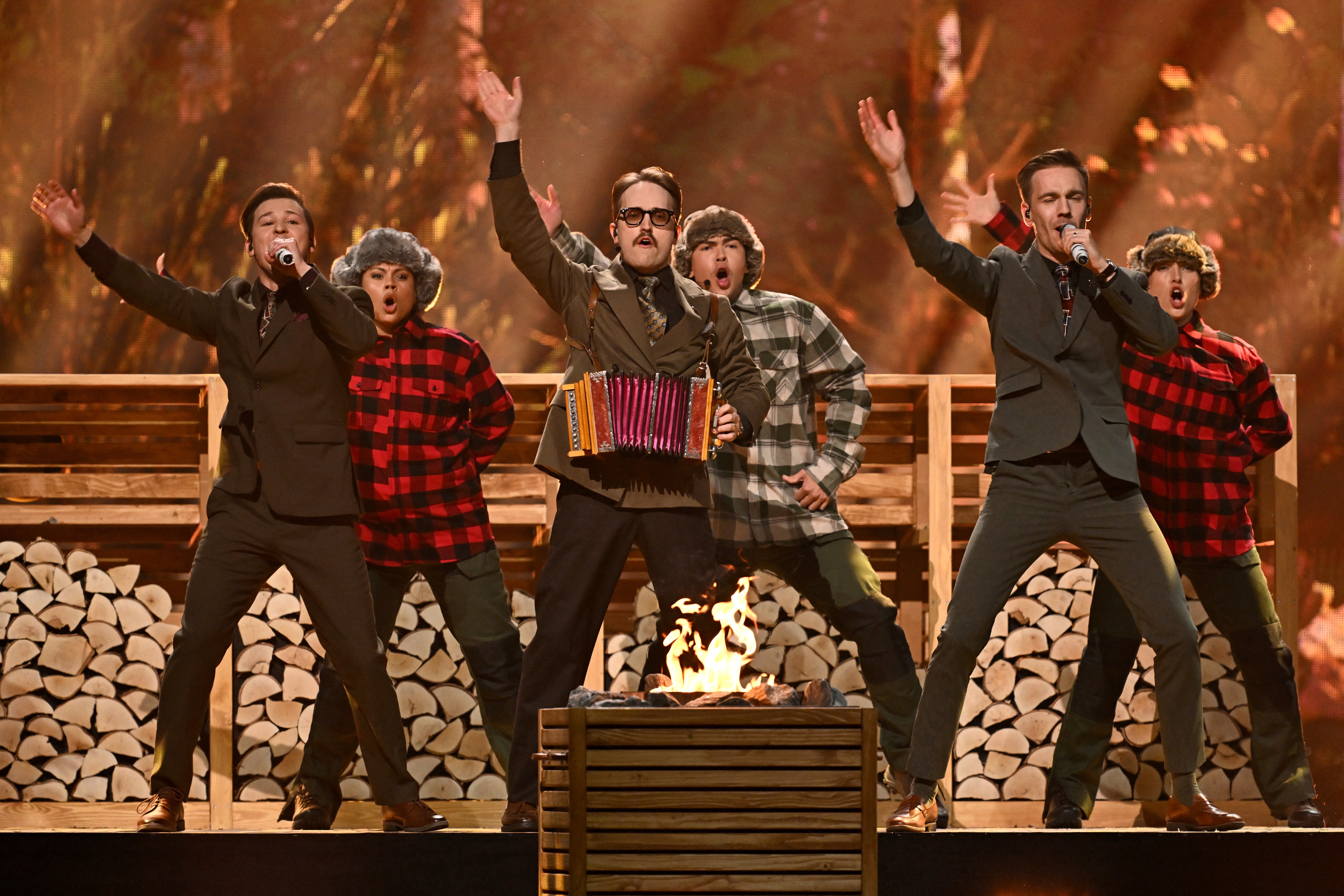 Musicians and dancers perform on the stage depicting wood and sauna seats.