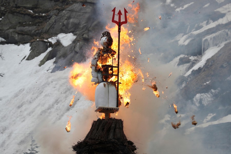 A large snowman figure is burned in an alpine setting.