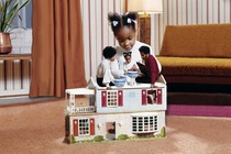 A young child plays with a doll version of her family in a dollhouse