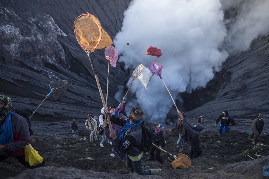 People stand just inside a volcanic crater, holding long nets, trying to catch offerings being tossed in.