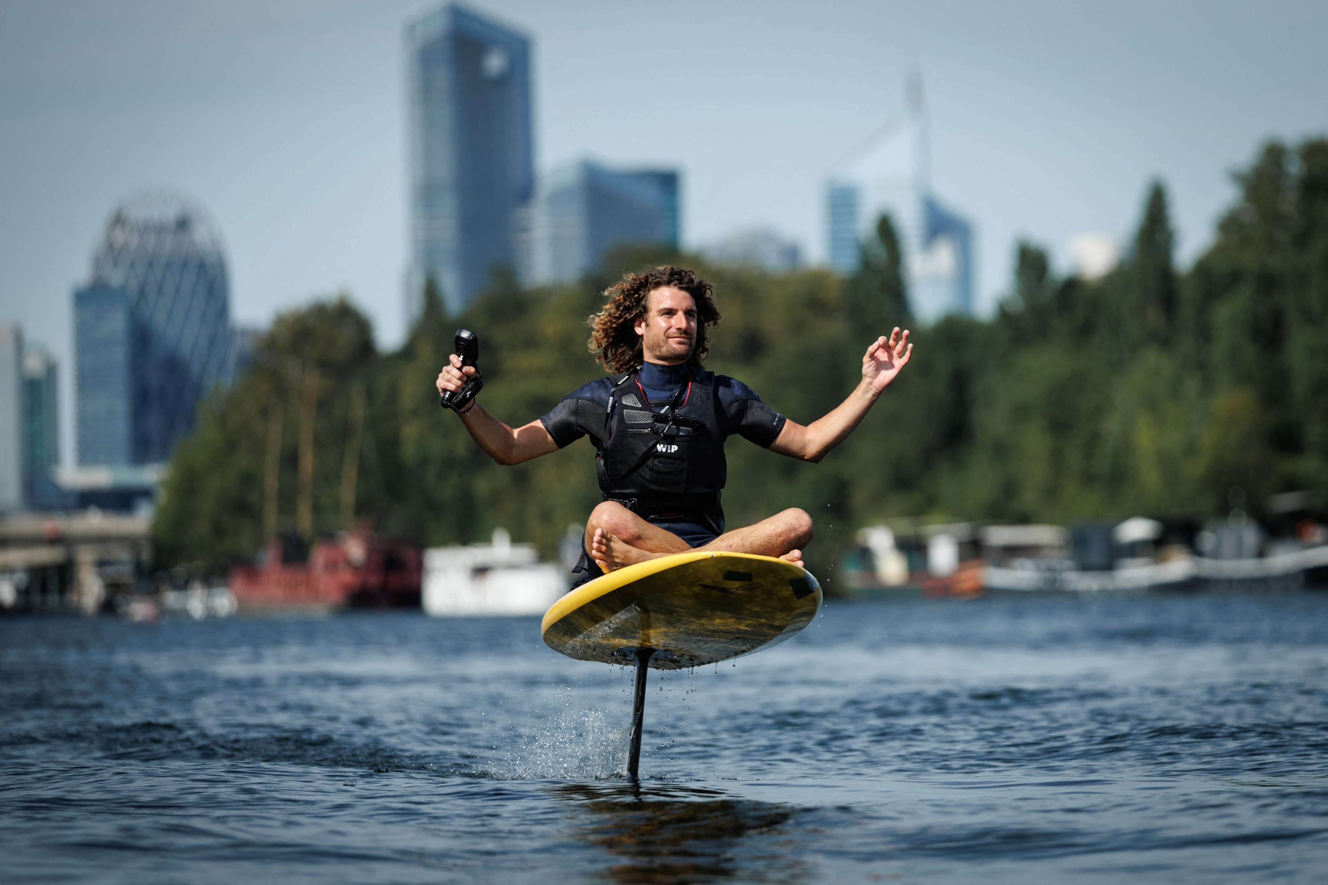 A person sits cross-legged on an e-foil board, riding down a river in Paris.