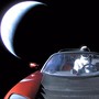 The dummy astronaut Starman, wearing a SpaceX space suit, in the driver's seat of a red Tesla Roadster in space as it speeds away from Earth