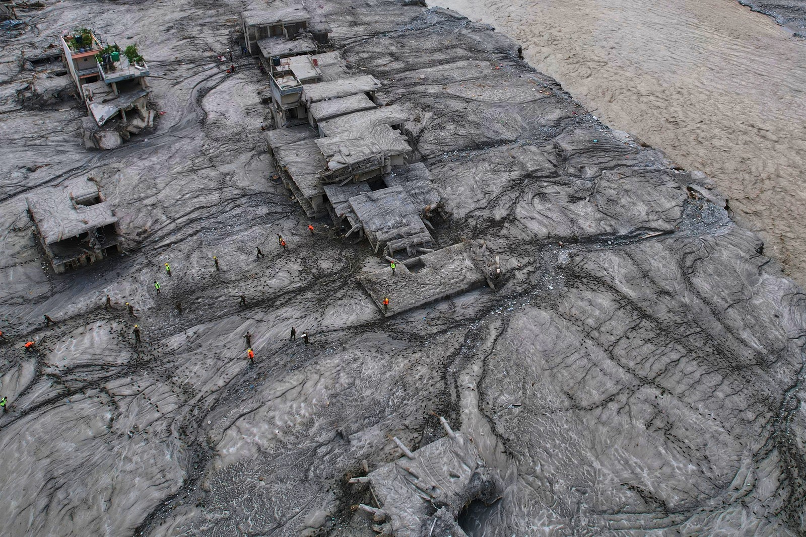 An aerial view of rescue workers inspecting damaged and mud-covered structures