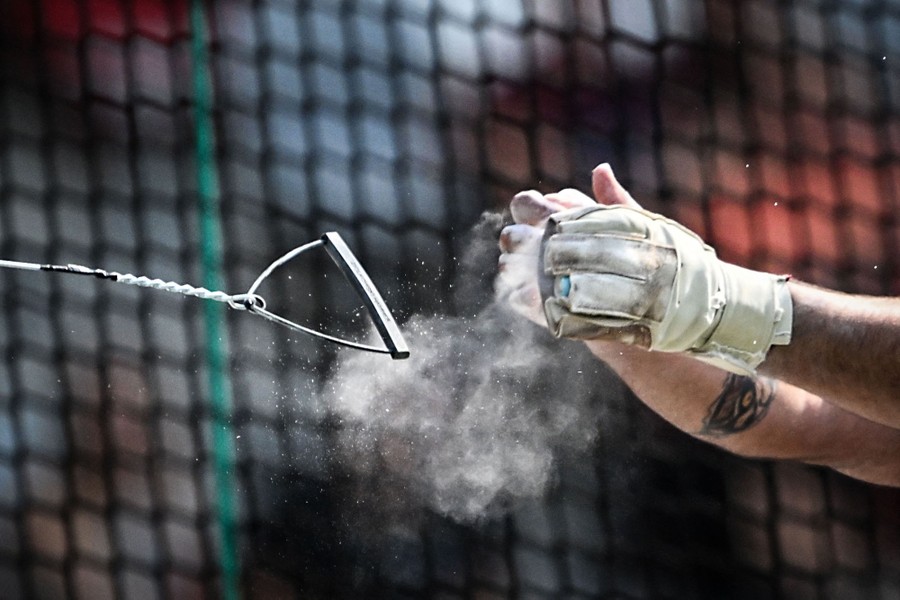 A close view of an athlete's gloved hands releasing the handle of a hammer, in a small cloud of chalk dust.