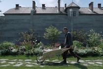 Christian Friedel as Rudolf pushing a wheelbarrow next to a wall with barbed wire