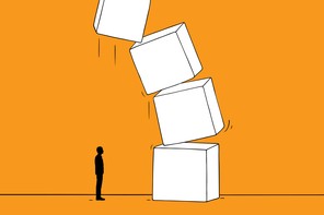 A small figure stands in front of a big stack of toppling boxes.
