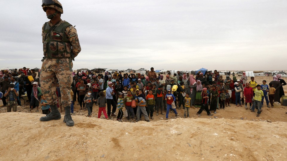 A Jordanian soldier stands guard as Syrian refugees, stuck between the Jordanian and Syrian borders, watch a group of them cross into Jordanian territory.