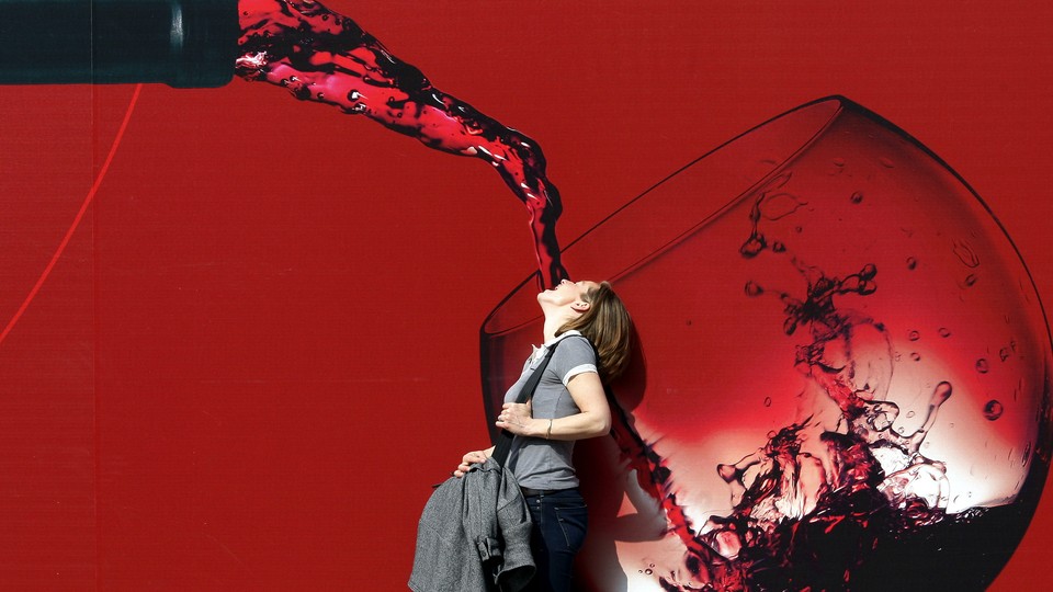 A woman stands with her mouth open in front of a large illustration of red wine being poured into a glass.