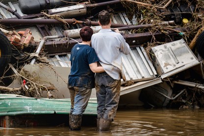 Two people stand in floodwater before wreckage in western North Carolina