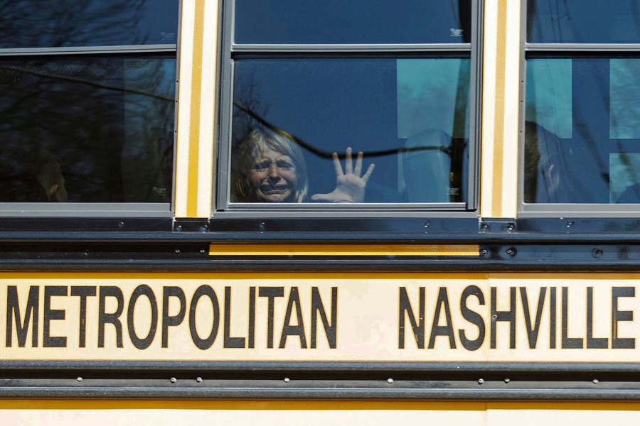 A child in a school bus weeps, looking out of a window.