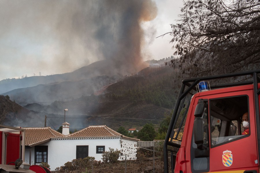 Firefighters sit in a truck with an eruption visible in the background.