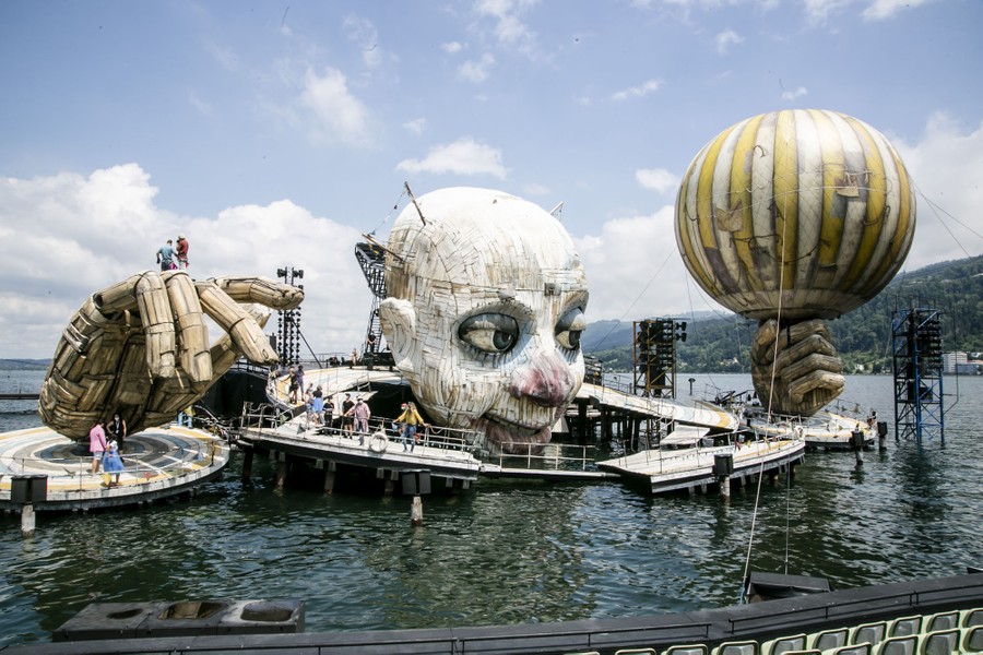 An enormous floating stage is seen, with sections shaped like a massive human head and two hands.