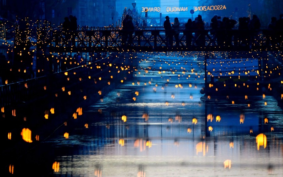 People walk on a bridge over a decorated canal.