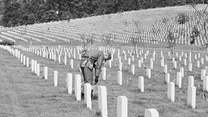 A black and white photograph of a soldier bowing before a hill of gravestones