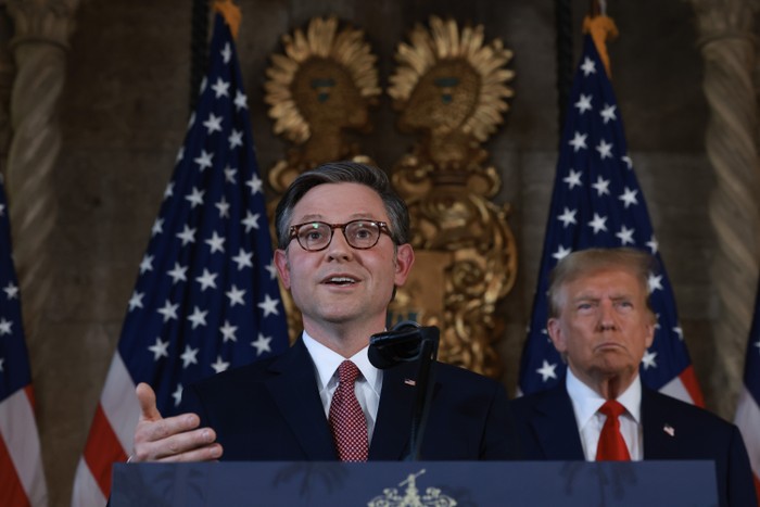 House Speaker Mike Johnson speaks at the podium and Donald Trump stands behind him