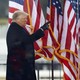 Donald Trump pointing, standing in front of American flags