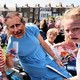 A man wearing Union Jack face paint and a woman wearing a King Charles face mask celebrate the coronation in a field while a child looks on, deeply distraught