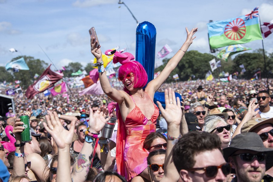 A woman sits on someone's shoulders, among a large crowd watching a concert.