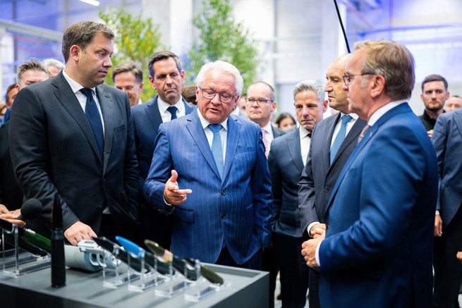Men stand around in a circle looking at items on a table