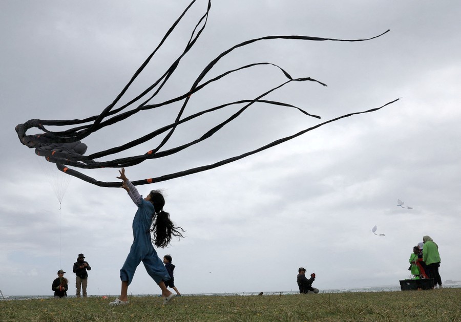 A girl stands in a grassy field, holding her arms up toward an octopus-shaped kite.