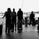 A black and white photo of travelers with suitcases wearing masks