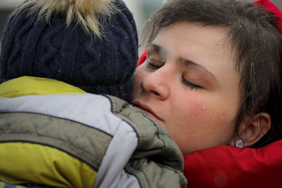 A person holds a small child close, outside, on a cold day.
