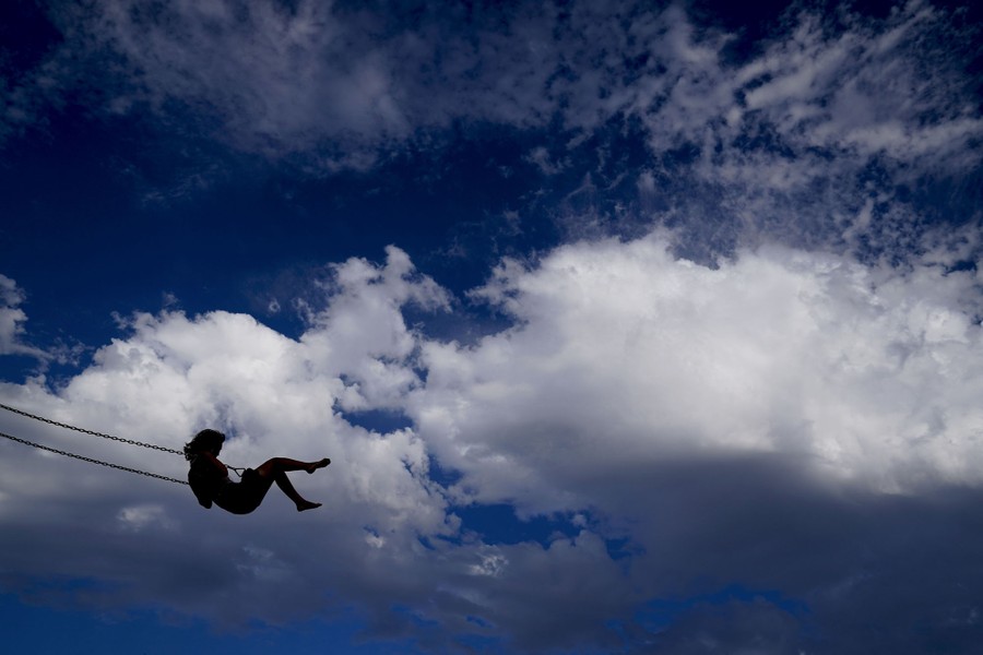 A woman swings against a cloudy sky.