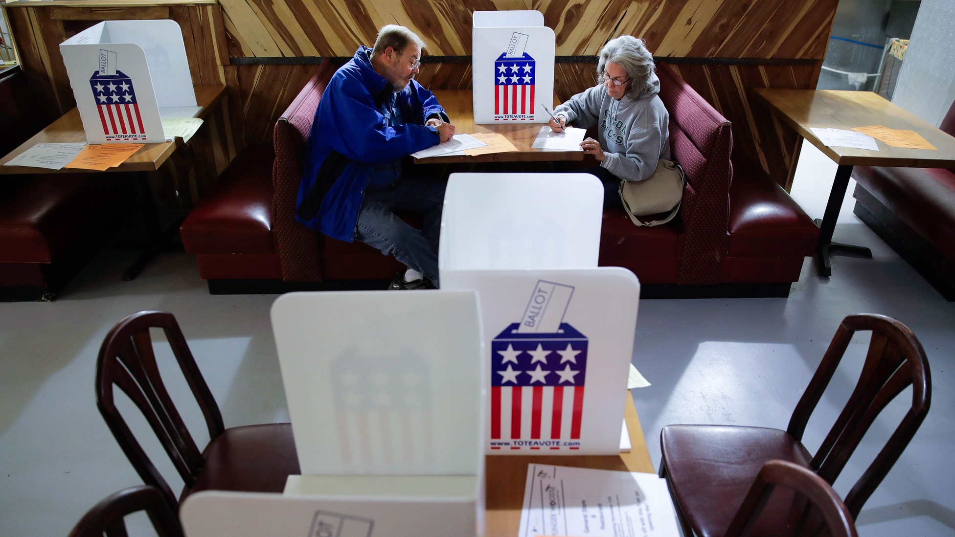 A man and a woman sitting across from each other in a booth filling out ballots