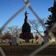 A photo of the Confederate Memorial in Arlington Cemetery, captured through a chain-link fence