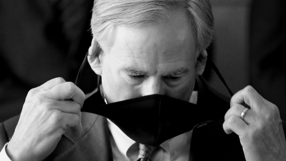 A black and white photo of Greg Abbott taking a mask off.