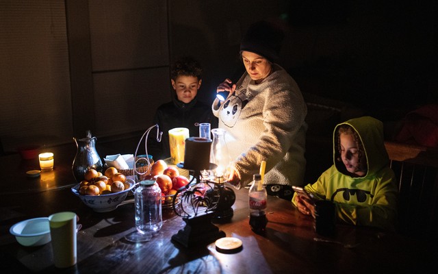 A woman adjusts an oil lamp in the dark while standing between her two sons