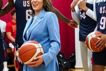A photograph of Kamala Harris holding a basketball, with members of the American Olympic men's basketball team seen in the background