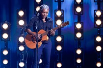 Tracy Chapman performing with a guitar at the Grammys, backdropped by stage lights