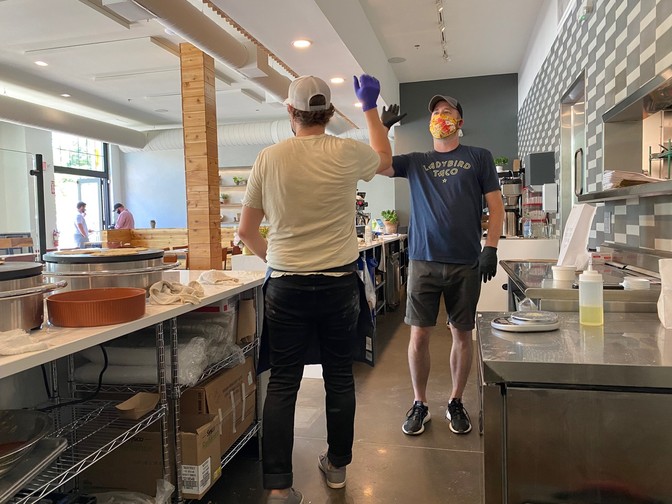 Two men mid-high five behind the counter at a restaurant