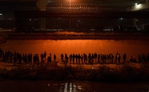 Migrants gathered at night in front of the border wall