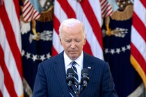 a photo of Joe Biden at a microphone, U.S. flags behind him, with his eyes closed