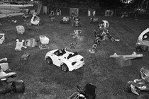 Children's toy cars, mowers, and other equipment strewn across a lawn