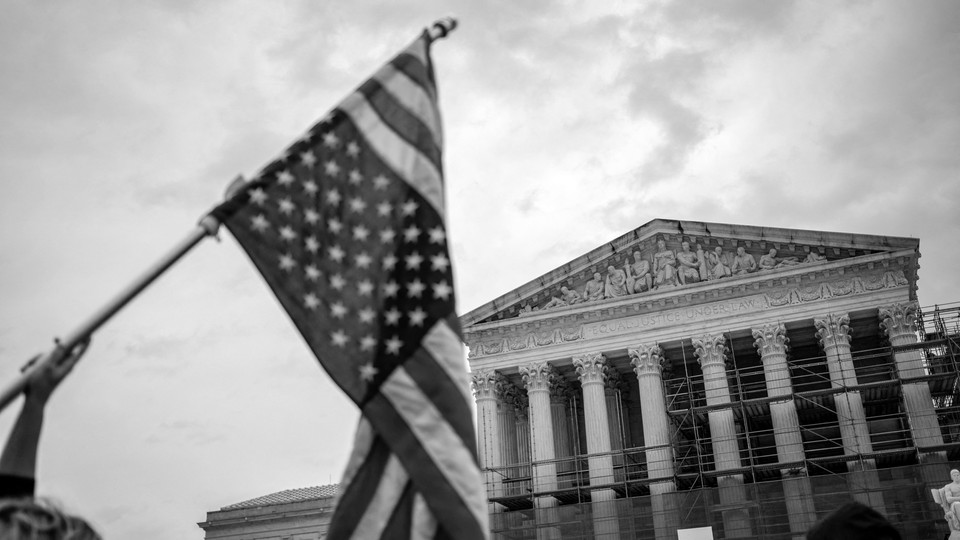 Person waving upside-down flag in front of Supreme Court building