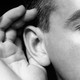 A man cups his hand to his ear