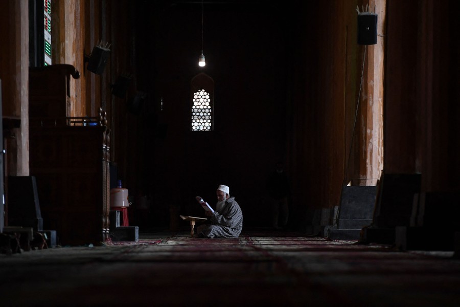 A man sits alone, reading, inside a large mosque.