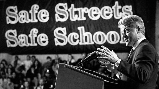 President Bill Clinton announces new initiatives to combat juvenile crime at the University of Massachusetts in Boston. A banner behind him reads 'Safe Streets; Safe Schools.'