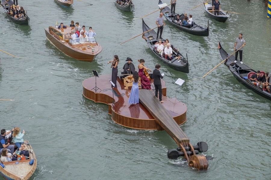A string quartet plays while standing on a boat shaped like a giant violin in Venice.