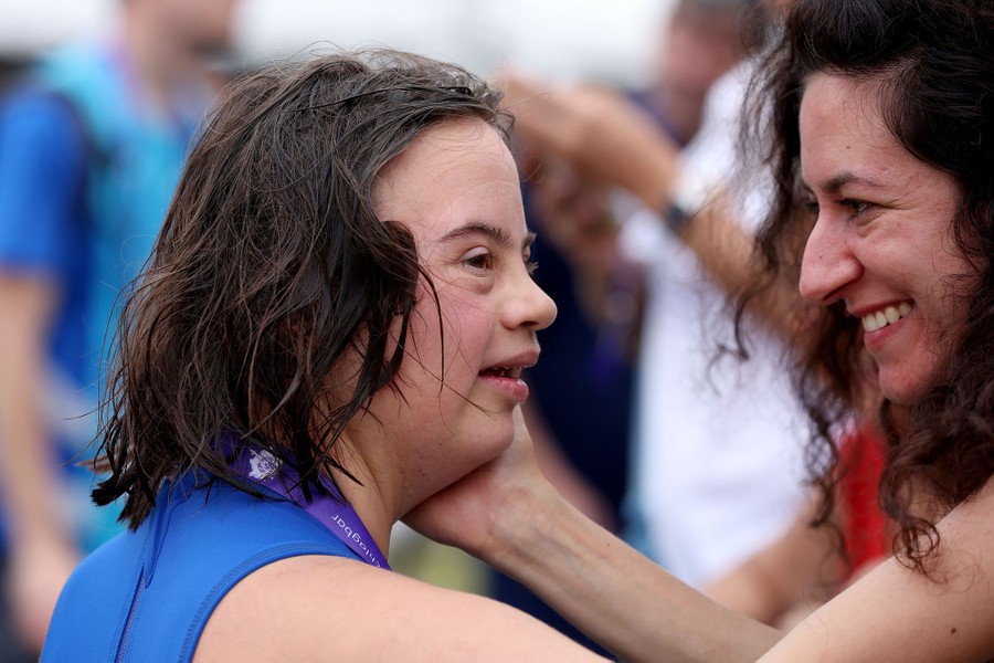A person smiles while holding the face of a tired swimmer, after a race.